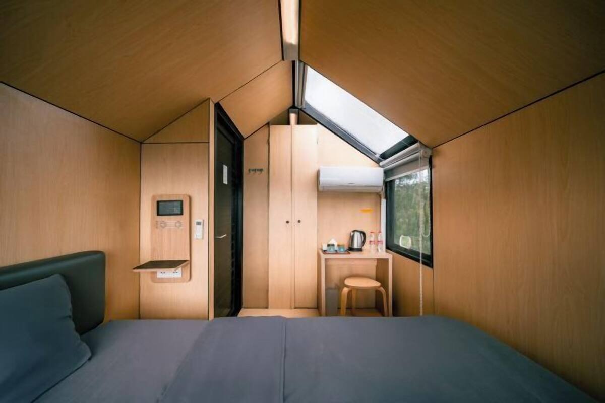 A compact room with a bed, a small desk, a chair, and a window.