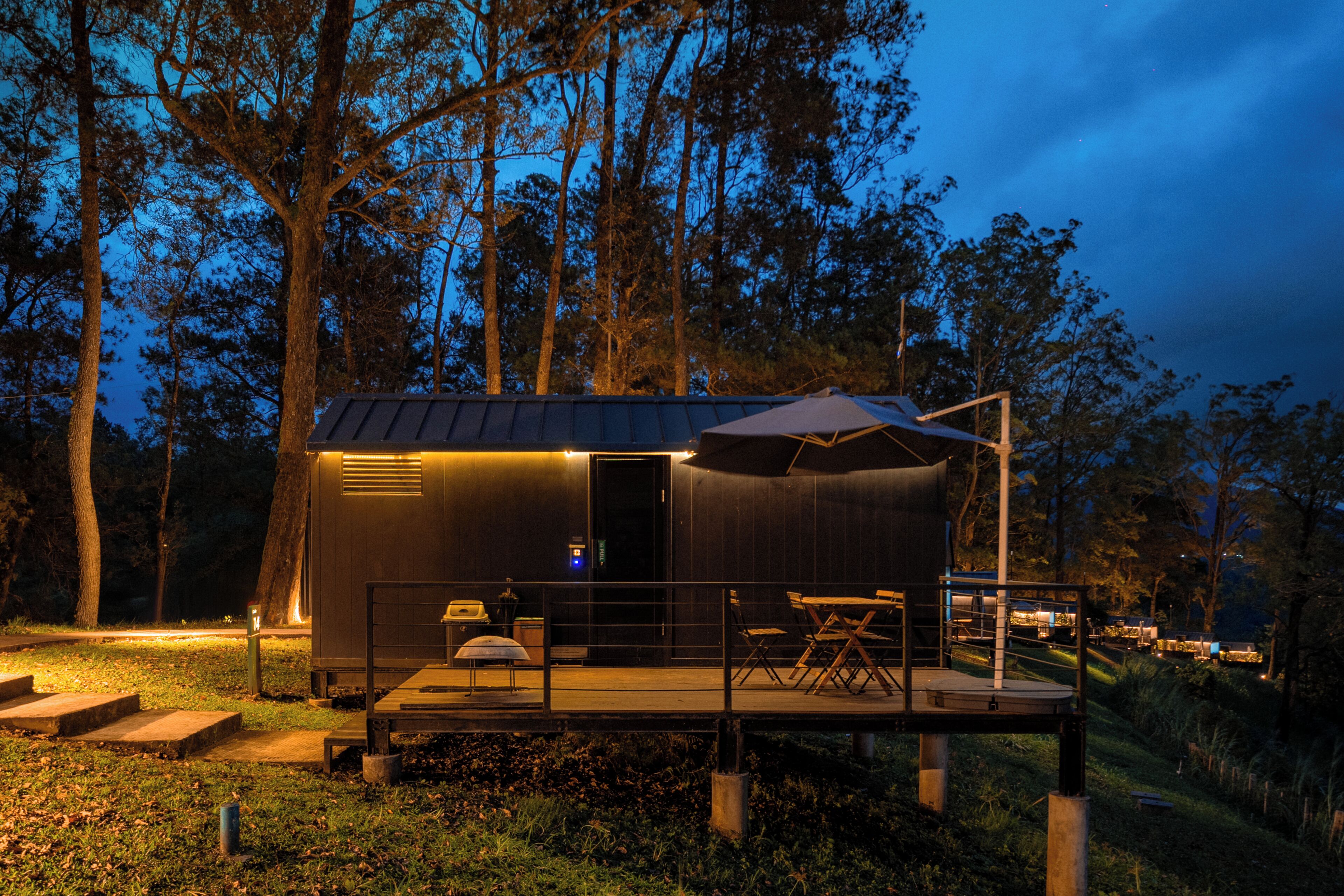 Eine kleine Holzhütte mit einer Terrasse, Sitzgelegenheiten im Freien und einem überdachten Bereich.