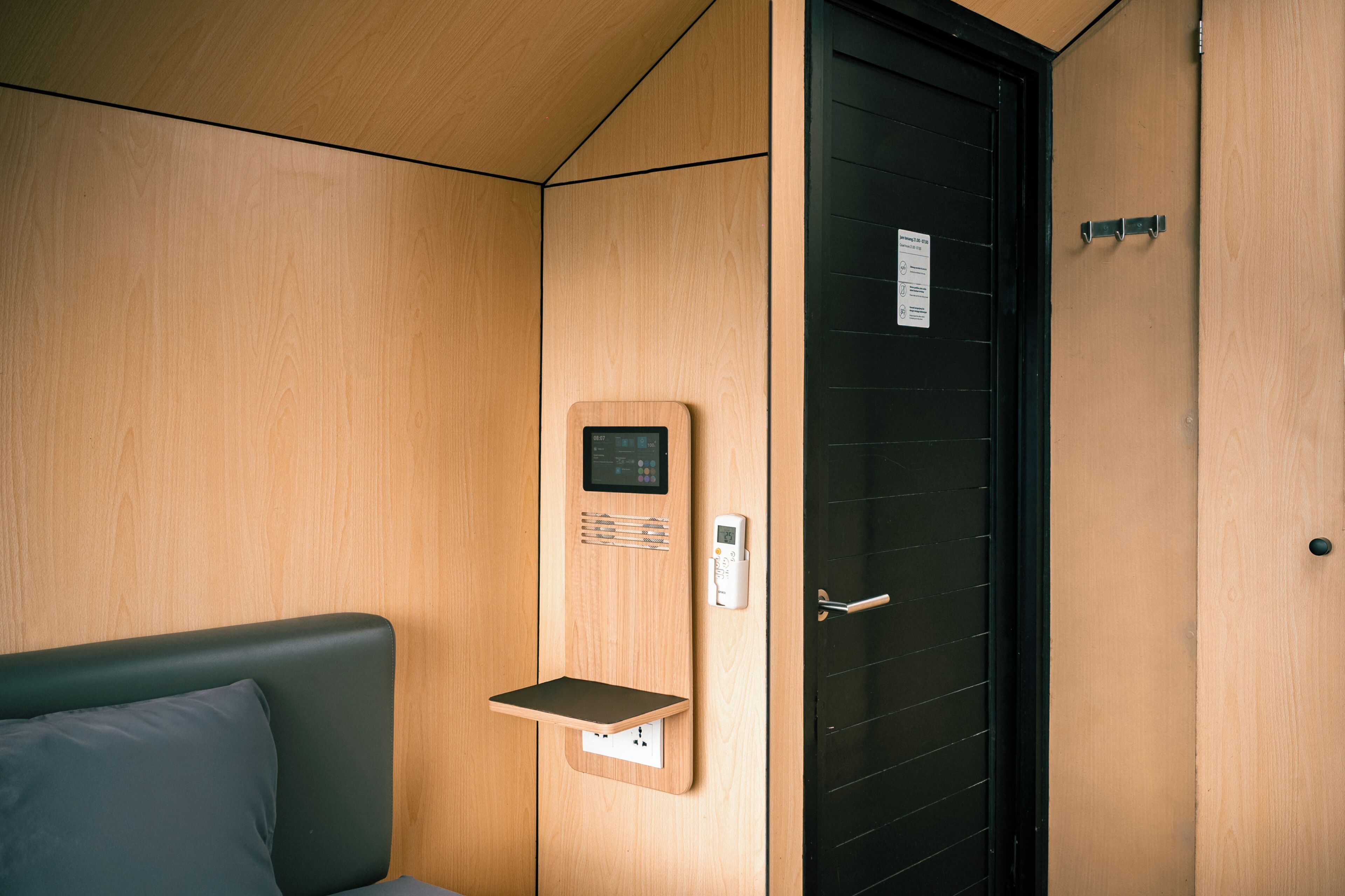 A wooden interior with a bed, a wall-mounted control panel, and a door with a handle.