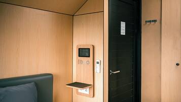 A wooden interior with a bed, a wall-mounted control panel, and a door with a handle.