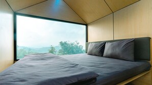 A modern bedroom with a large window, a bed with grey bedding, and wooden walls. - Bobocabin Coban Rondo Malang (Pujon)