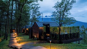 A secluded cabin with a pathway leading to the entrance, surrounded by trees and overlooking a mountainous landscape. - Bobocabin Coban Rondo Malang (Pujon)