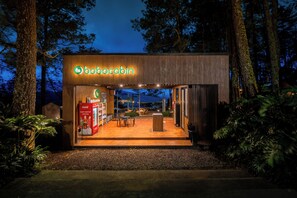 Un Bobocabin moderne et bien éclairé, doté d’un réfrigérateur Coca-Cola, d’une façade en bois et offrant une vue sur la forêt environnante.