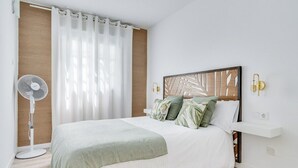 Un dormitorio con cama, ventilador, cabecera de madera y una lámpara fijada a la pared.