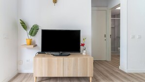 Una sala de estar moderna con un televisor de pantalla plana sobre un mueble de madera, una planta en un estante y una puerta que da a un baño.