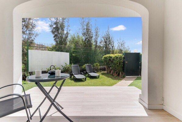 A patio with a table and chairs, a small lawn, and a green fence.