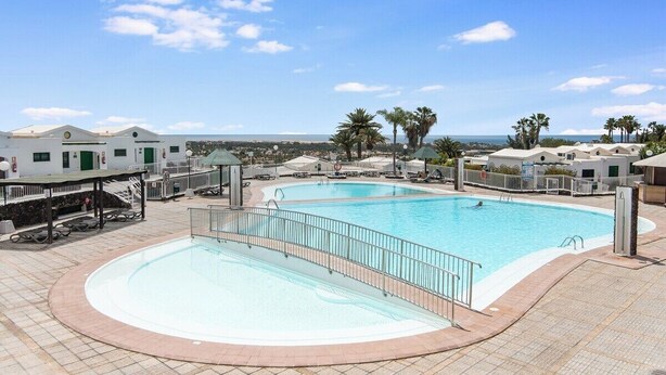 Una piscina de borde curvo, rodeada por una terraza con baldosas y una barandilla.
