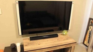 Ein Flachbildfernseher an einem Holzboden, mit Fernbedienung und einem kleinen Ventilator daneben.