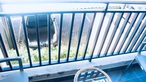 Ein Balkon mit Metallgeländer, einem blauen Fliesenboden und einem kleinen, runden Tisch mit Glasplatte.