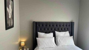 Ein ordentlich bezogenes Bett mit einer gebügelten Kopfstütze, einer Nachttischlampe und einem gerahmten Bild an der Wand.