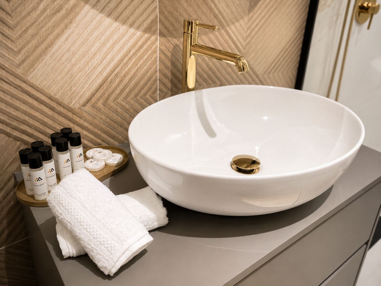 A bathroom with a white sink, gold faucet, and toiletries on a tray.