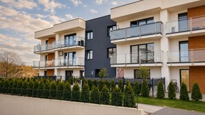 A modern multi-story residential building with balconies, a flat roof, and a landscaped front yard.