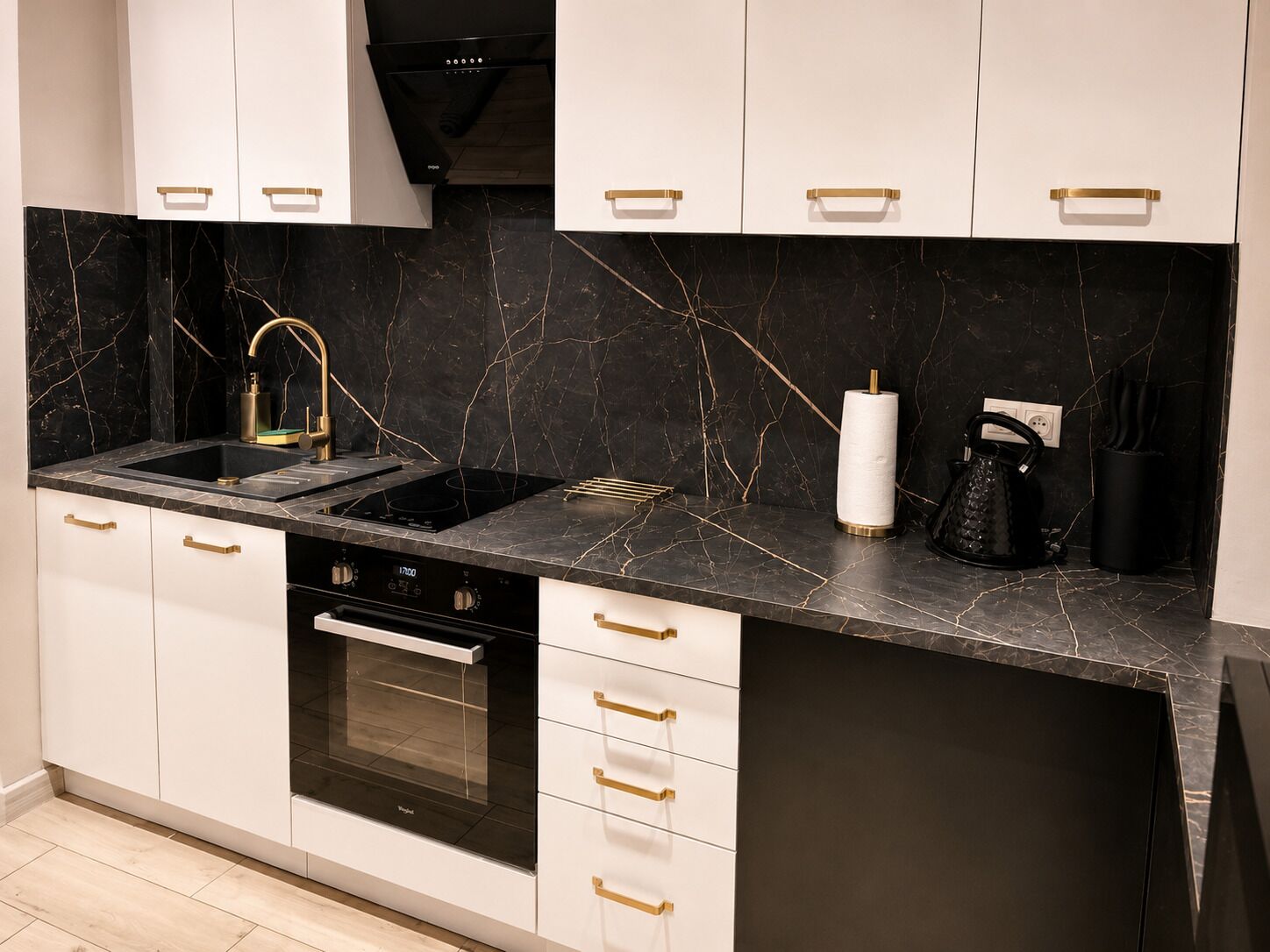 Una cocina moderna con armarios blancos, salpicadero de mármol negro y tiradores dorados.