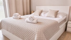 A neatly made bed with a quilted cover, two pillows, and rolled towels on the side.
