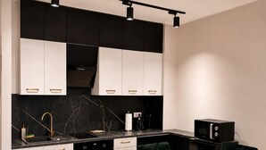 A modern kitchen with white and black cabinetry, a marble countertop, and a dining area with a white table and dark green chairs.