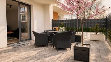A patio with outdoor furniture, a small tree with pink blossoms, and a black fence.