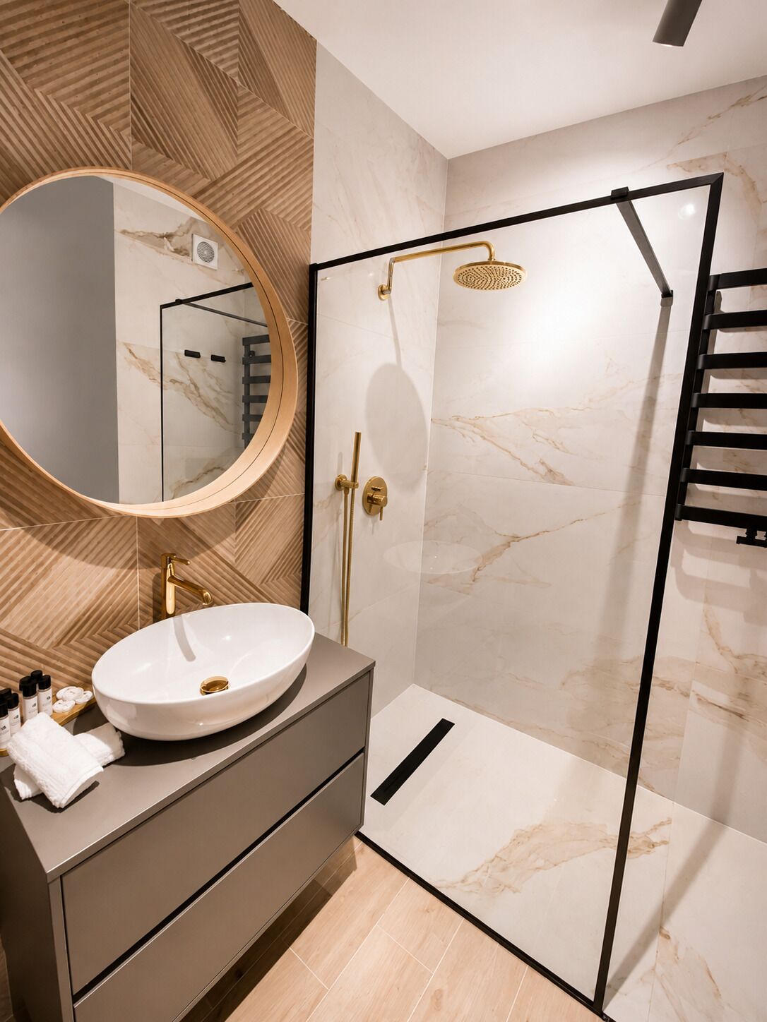 A modern bathroom with a round mirror, a white sink, a walk-in shower, and a wooden wall panel.