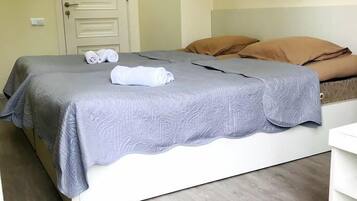 A neatly made bed with a grey bedspread and rolled towels, a white bedside table, and a wooden floor.