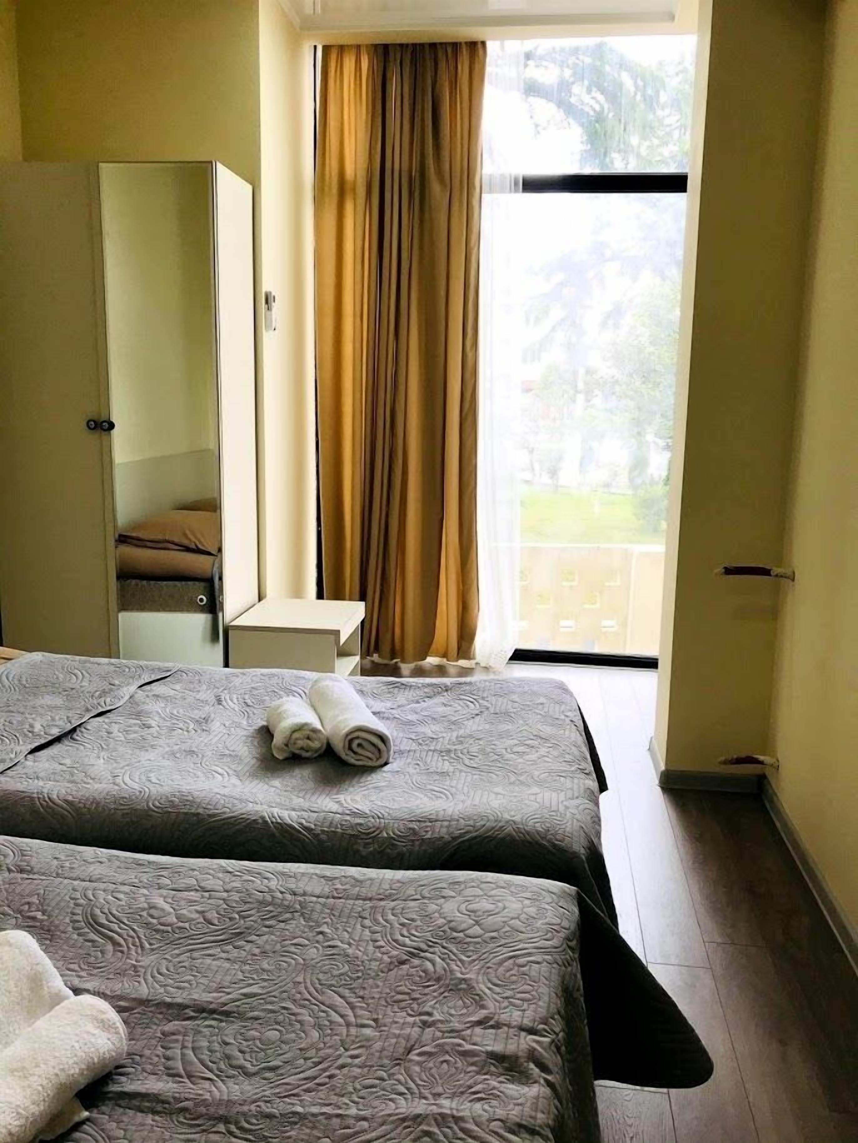 Habitació d'hotel amb dos llits, un armari, una taula petita i vista a l'exterior a través d'una finestra amb cortines.