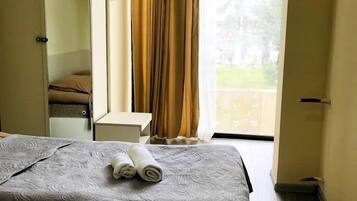 Habitació d'hotel amb dos llits, un armari, una taula petita i vista a l'exterior a través d'una finestra amb cortines.