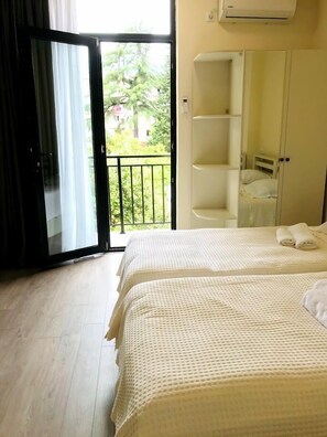 A bedroom with two beds, a wardrobe, and a balcony with a view of greenery. - Hotel Gurya (Kobuleti)