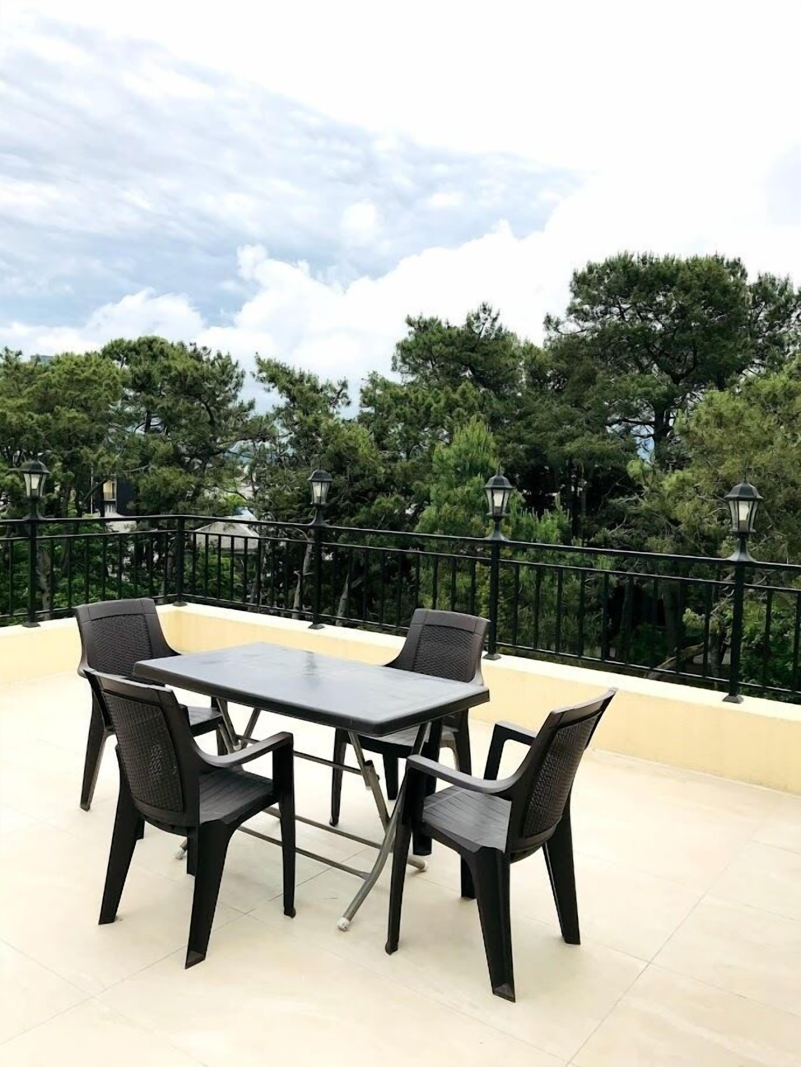 Terraza en la azotea con mesa y sillas, rodeada por una barandilla negra y árboles al fondo.
