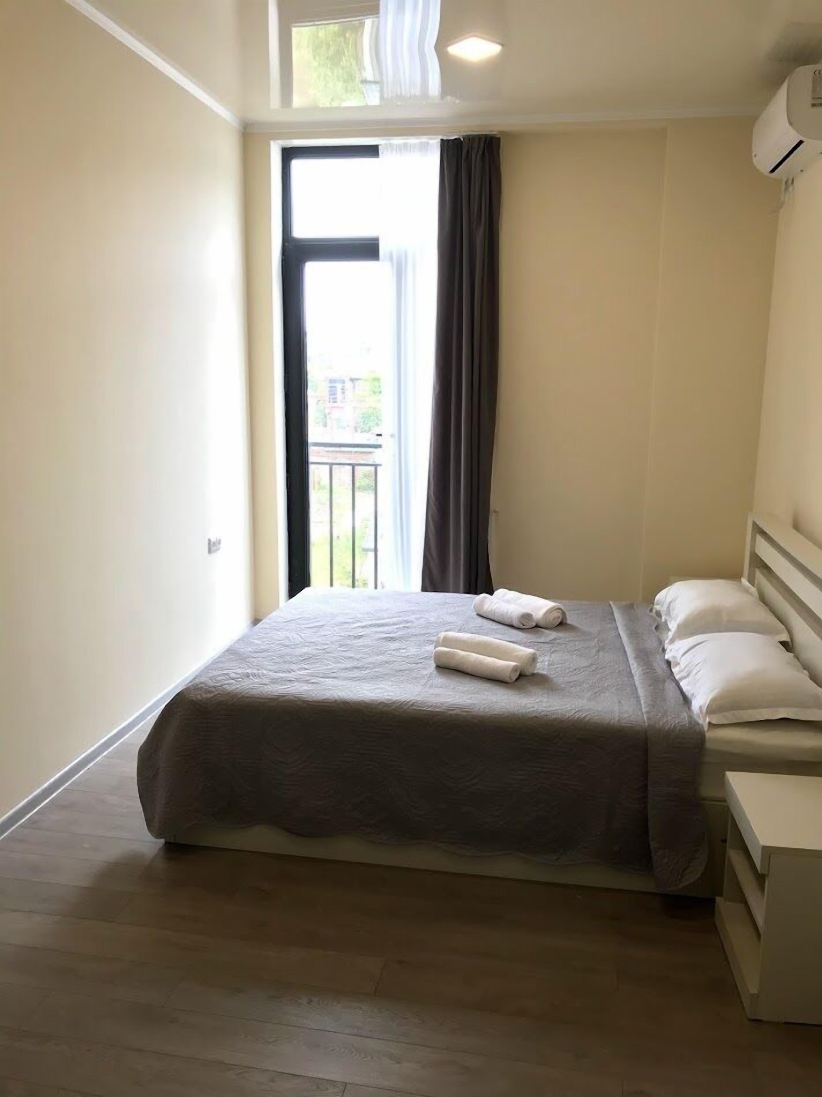 A hotel room with a bed, a nightstand, a window with curtains, and an air conditioning unit.