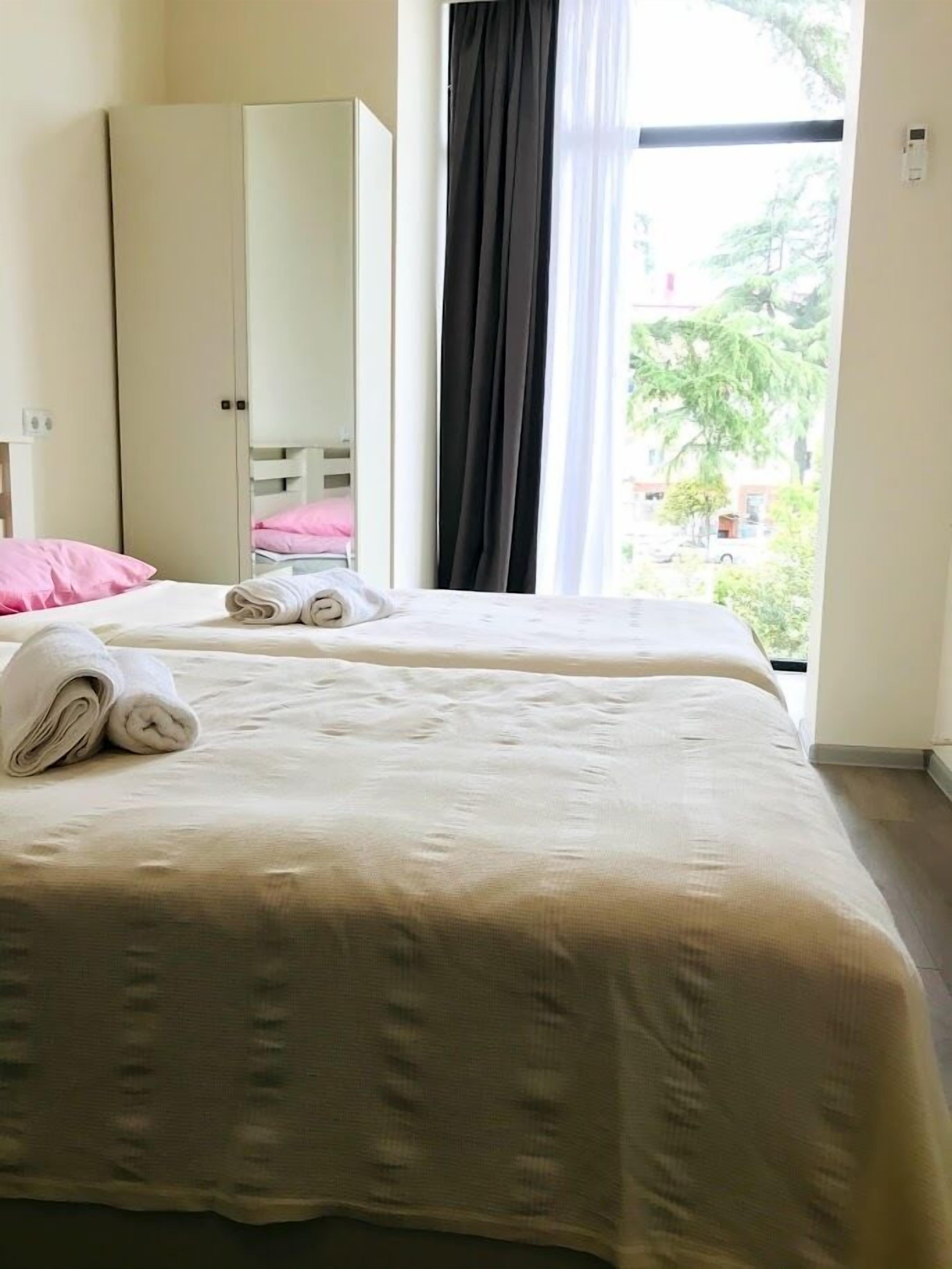 Cama bem arrumada com toalhas dobradas, um guarda-roupa e uma janela com cortinas.