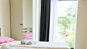 A neatly made bed with rolled towels, a wardrobe, and a window with curtains. - Hotel Gurya (Kobuleti)