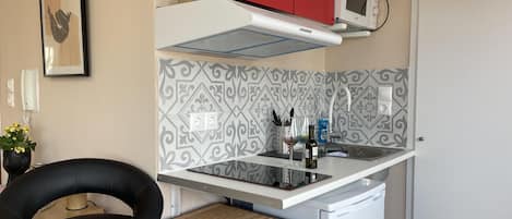 A compact kitchen with a microwave, a red cabinet, and a patterned backsplash.