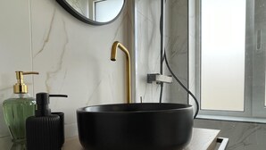 A black vessel sink with a gold faucet on a wooden countertop, a green glass bottle, and a black pump bottle. - Cozy Apartment in Heart Athens Near Metro Fix 100m (Athens)