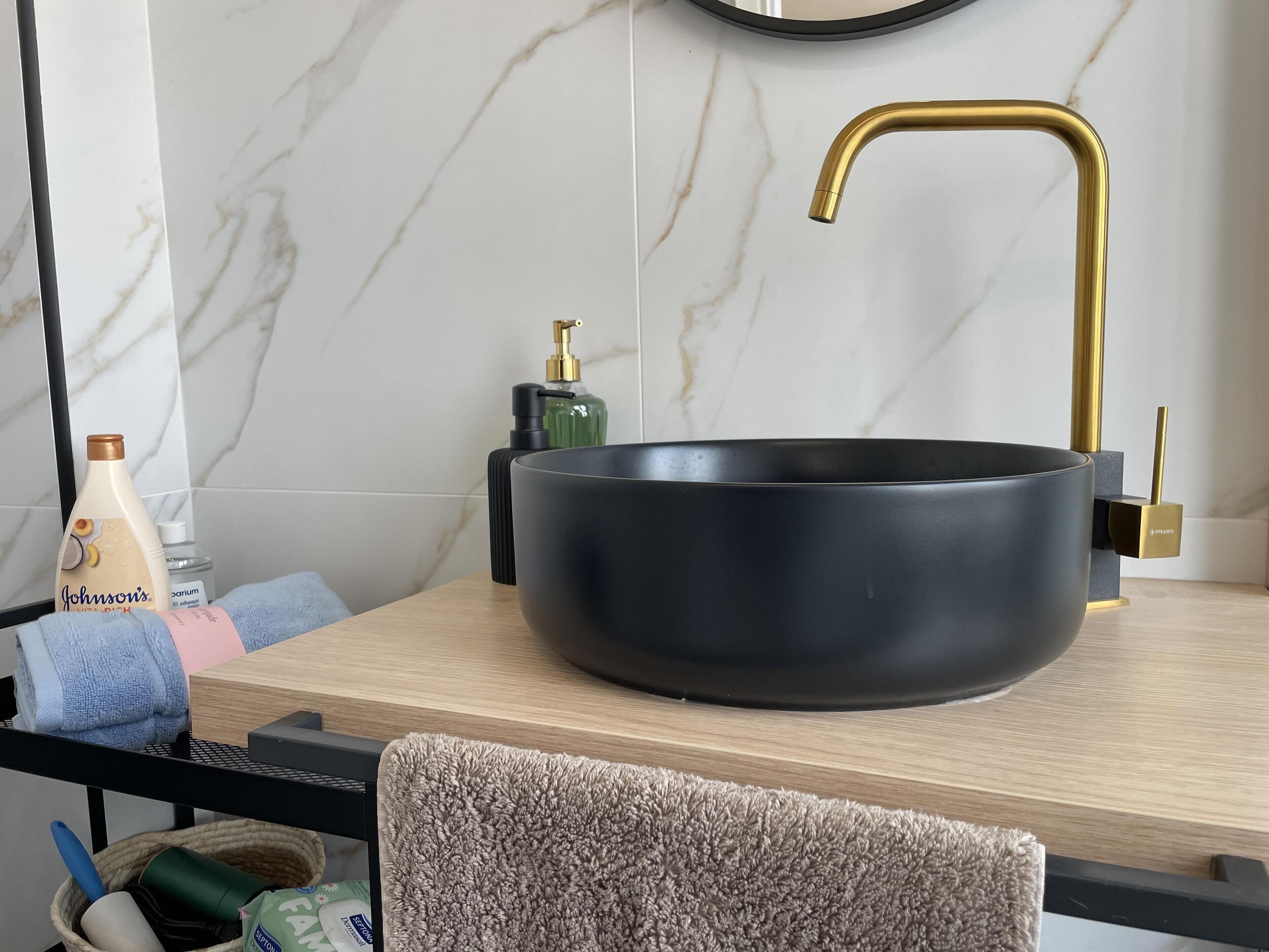 A bathroom with a black vessel sink, a gold faucet, and toiletries on the counter.