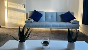 A modern living room with a grey sofa, two blue cushions, a painting of trees, and two potted plants on a white coffee table. - Spacious 3-bed House in Swindon (Swindon)