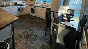 A compact kitchen with a dining area, a washing machine, and a window providing natural light. - Spacious 3-bed House in Swindon (Swindon)