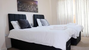 Ein Hotelzimmer mit zwei Betten, weißer Bettwäsche und einem Stadtbild an der Wand.