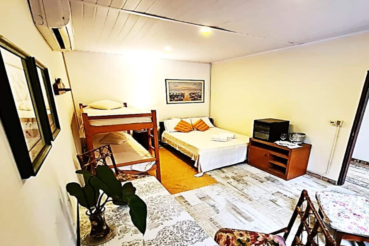 A compact room with a bunk bed, a single bed, a small table, and a television.