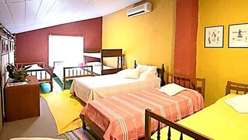 A small, cozy room with two single beds, a wooden table, a small desk, and a window.