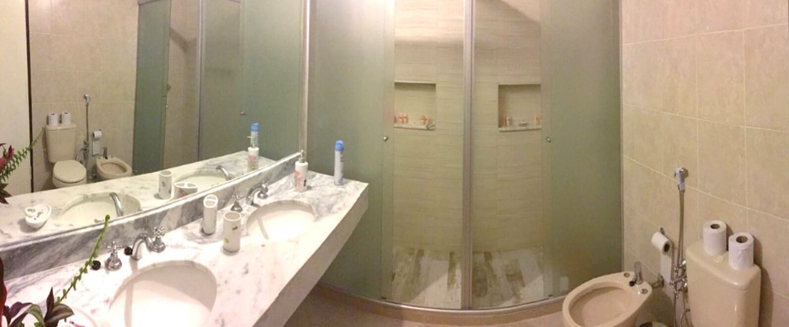 A bathroom with a marble vanity, a glass shower enclosure, and two toilets.