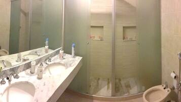 A bathroom with a marble vanity, a glass shower enclosure, and two toilets.