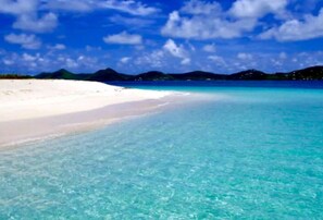 A beach with clear turquoise water and white sand, surrounded by mountains.