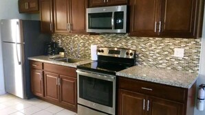 Una cocina con armarios de madera oscura, electrodomésticos de acero inoxidable, salpicadero de azulejos y encimera de granito.