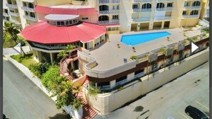 Un hotel con piscina, varios balcones y un edificio de techo rojo curvo.
