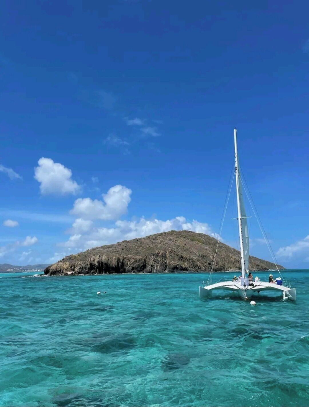 Un voilier sur des eaux turquoise, avec une île rocheuse en arrière-plan.