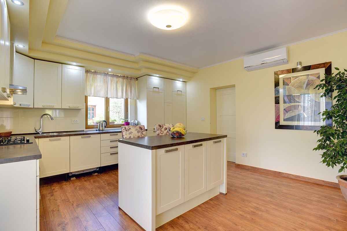 Une cuisine moderne avec des meubles blancs, un îlot central et une grande fenêtre agrémentée de rideaux.