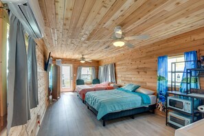 A wooden cabin room with two beds, a ceiling fan, a microwave, and a window with curtains. - 1 Mi to Ocean: Colorful Freeport Beach Rental! (Freeport)