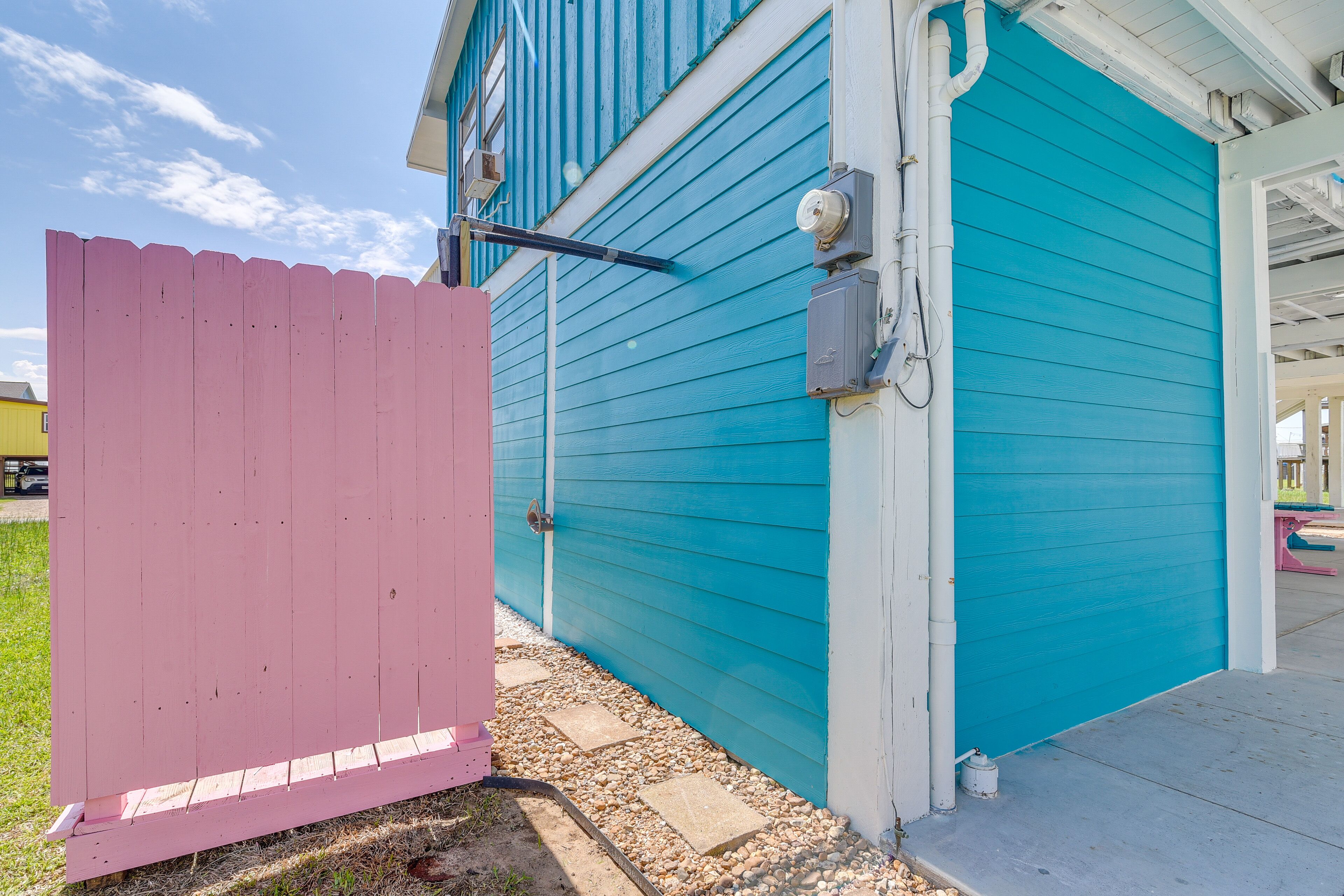 A house with a teal exterior, a pink fence, and a visible garage door.