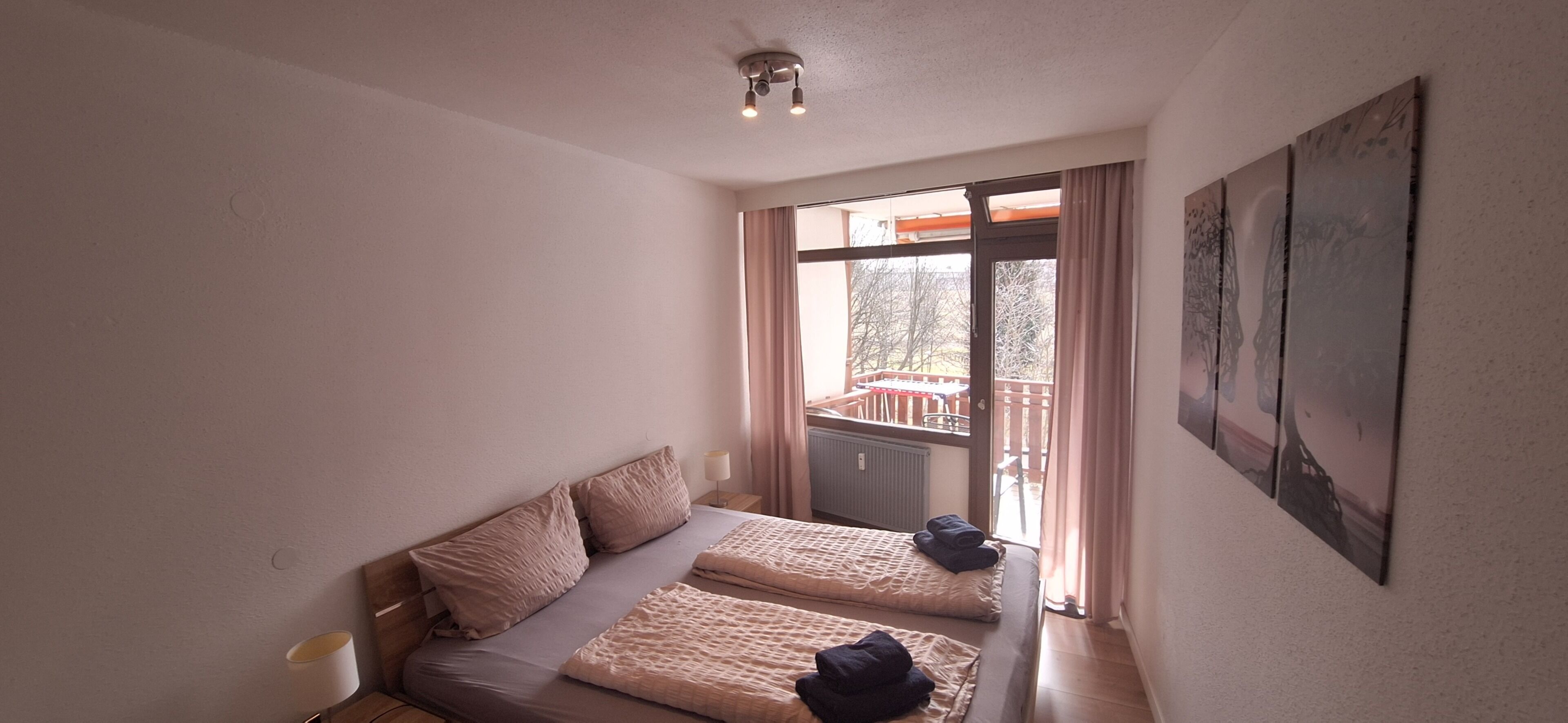 Ein Schlafzimmer mit zwei Betten, einem Fenster mit Vorhängen, einer Deckenleuchte und einem an der Wand befestigten Kunstwerk.