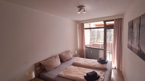 Quarto com duas camas, janela com cortinas, luminária no teto e uma obra de arte na parede.