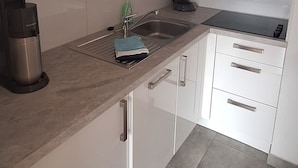 Uma cozinha moderna com armários brancos, uma cafeteira de aço inoxidável e uma chaleira elétrica preta.