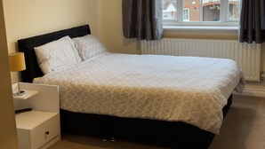 Uma cama bem arrumada com um edredom estampado com padrão geométrico, uma mesa de cabeceira com abajur e uma janela com cortinas.